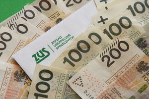 Na zdjęciu widać banknoty polskie oraz kopertę z logo ZUS. Dominują nominały 100 i 200 złotych.