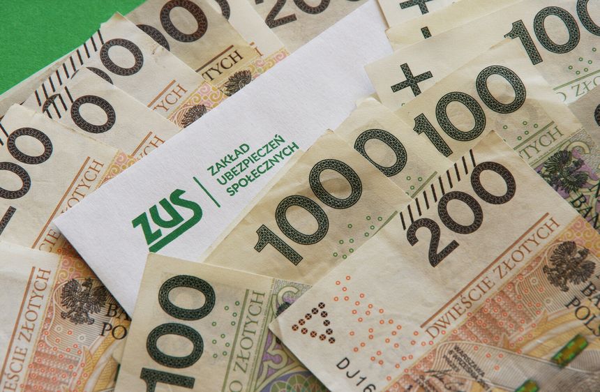 Na zdjęciu widać banknoty polskie oraz kopertę z logo ZUS. Dominują nominały 100 i 200 złotych.