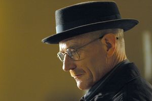 Mężczyzna w kapeluszu, z okularami i wąsami, patrzy w bok, na tle jednolitej ściany.