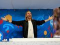 Na zdjęciu David Guetta w czarnym ubraniu, unoszący ręce, w tle kolorowa scenografia.