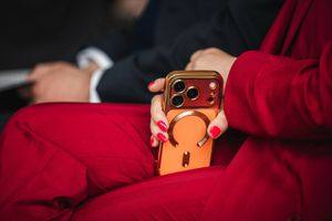 Kobieta w czerwonym garniturze trzyma złoty telefon z pomarańczowym etui.