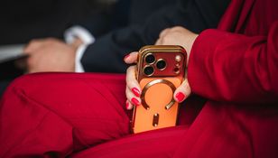 Kobieta w czerwonym garniturze trzyma złoty telefon z pomarańczowym etui.
