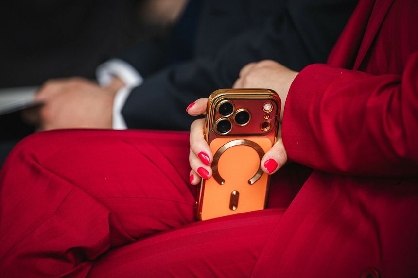 Kobieta w czerwonym garniturze trzyma złoty telefon z pomarańczowym etui.