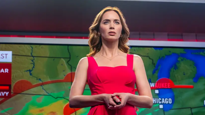 Na zdjęciu kobieta w różowej sukience stoi przed mapą pogodową, prezentując prognozę.