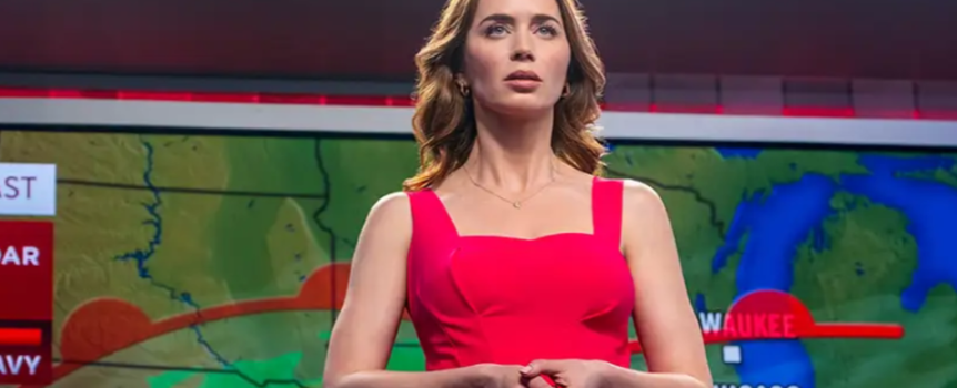 Na zdjęciu kobieta w różowej sukience stoi przed mapą pogodową, prezentując prognozę.
