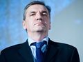 Na zdjęciu mężczyzna w garniturze, z poważnym wyrazem twarzy, na tle jasnoniebieskiego tła.
