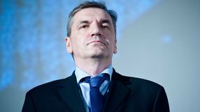 Na zdjęciu mężczyzna w garniturze, z poważnym wyrazem twarzy, na tle jasnoniebieskiego tła.