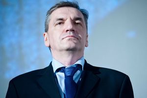 Na zdjęciu mężczyzna w garniturze, z poważnym wyrazem twarzy, na tle jasnoniebieskiego tła.