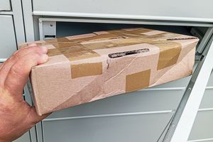 Opis ALT: Ręka trzyma pudełko z taśmą, wkładane do otworu w szarym, metalowym skrzynce.