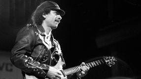 Mężczyzna w skórzanej kurtce gra na gitarze, na tle ciemnej sceny.