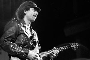 Mężczyzna w skórzanej kurtce gra na gitarze, na tle ciemnej sceny.