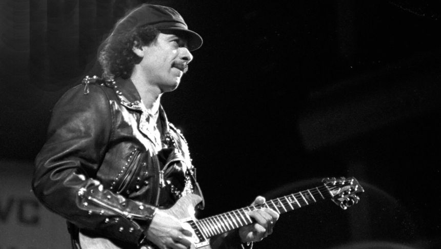 Mężczyzna w skórzanej kurtce gra na gitarze, na tle ciemnej sceny.
