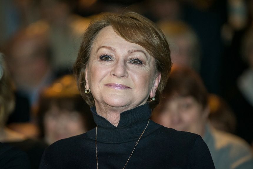 Uśmiechnięta kobieta w czarnej bluzce, z krótkimi włosami, w tle rozmyte twarze.