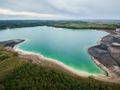 Zdjęcie przedstawia jezioro wśród zielonych terenów i sztucznych plaż. Woda o turkusowym kolorze.