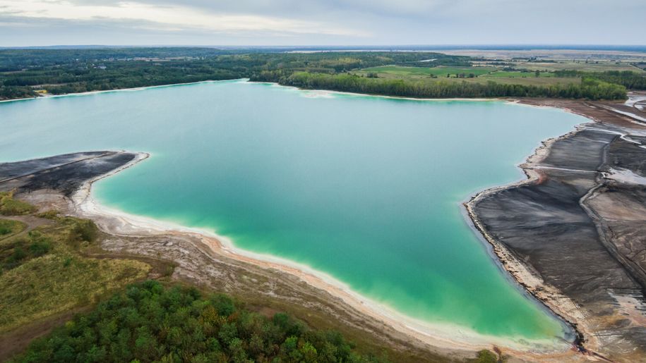 Zdjęcie przedstawia jezioro wśród zielonych terenów i sztucznych plaż. Woda o turkusowym kolorze.