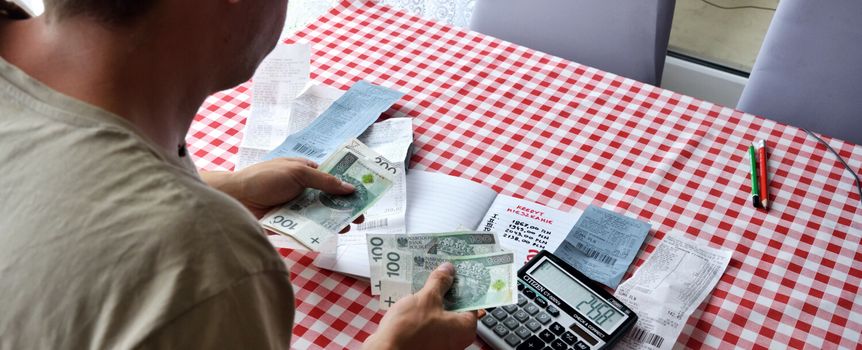 Mężczyzna liczy pieniądze przy stole, z widocznymi rachunkami i kalkulatorem.