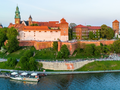Widok na Wawel, zamek na wzgórzu, z rzeką i spacerującymi ludźmi w tle.