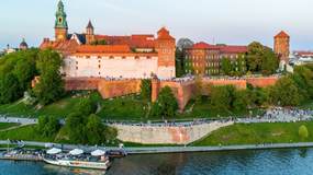 Widok na Wawel, zamek na wzgórzu, z rzeką i spacerującymi ludźmi w tle.