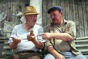 Dwaj mężczyźni w kapeluszach rozmawiają na ławce, trzymając przedmioty w rękach.