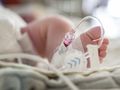 Zdjęcie przedstawia stopę noworodka z rurkami medycznymi w otoczeniu szpitalnym.