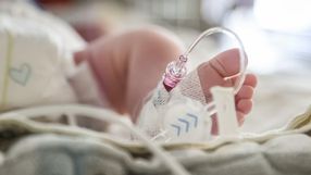 Zdjęcie przedstawia stopę noworodka z rurkami medycznymi w otoczeniu szpitalnym.