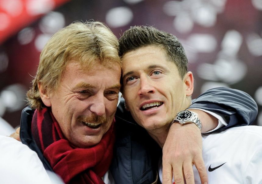 Zbigniew Boniek i Robert Lewandowski przytulają się, celebrując radośnie. W tle rozmyte kolory i konfetti.