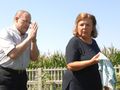 Dwoje ludzi w polu, mężczyzna złożonymi dłońmi, kobieta z szarfą w ręku. Tło: kukurydza.