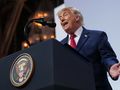 Mężczyzna w garniturze mówi do mikrofonu, na tle podium z godłem USA.