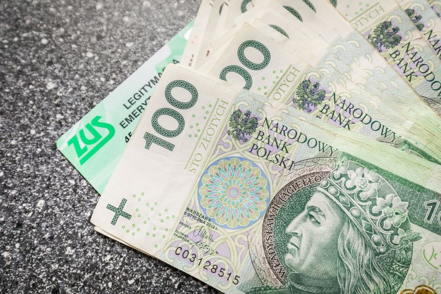 Na zdjęciu widać banknoty 100 zł i kartę ZUS na ciemnym tle.