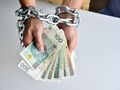 Ręce związaną łańcuchami trzymają banknoty; wizualizacja ograniczeń finansowych.
