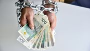 Ręce związaną łańcuchami trzymają banknoty; wizualizacja ograniczeń finansowych.