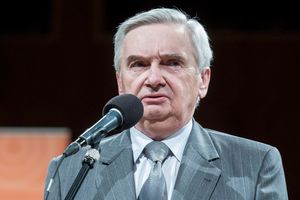Mężczyzna w szarym garniturze mówi do mikrofonu, wygląda poważnie. Tło rozmyte.