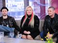 Trzy osoby siedzą na kanapie, w tle widać okna. Na stole szklanki z wodą i żółte kwiaty.