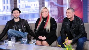 Trzy osoby siedzą na kanapie, w tle widać okna. Na stole szklanki z wodą i żółte kwiaty.