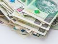 Stos pieniędzy w różnych nominałach na białym tle, widać banknoty o wartości 100 i 200 zł.