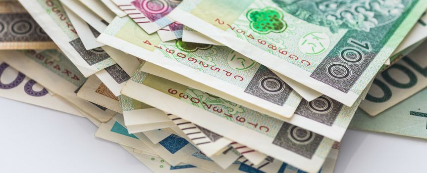 Stos pieniędzy w różnych nominałach na białym tle, widać banknoty o wartości 100 i 200 zł.
