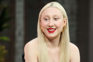Kobieta z długimi, jasnymi włosami, w modnych kolczykach i czerwonej pomadce, uśmiecha się.