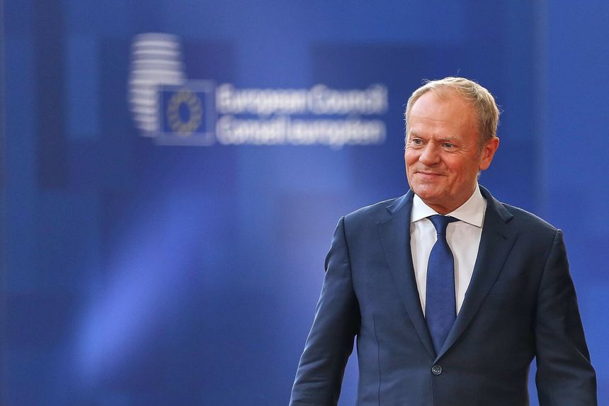 Mężczyzna w garniturze uśmiecha się na tle niebieskiej ścianki z logo Rady Europejskiej.