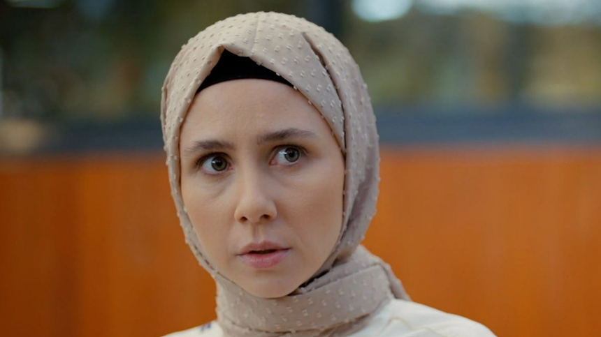Kobieta w jasnym hijabie z poważnym wyrazem twarzy, patrzy w stronę kamery.