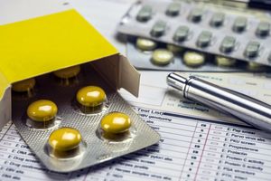 Opis ALT: Żółte tabletki w blistrze na tle formularzy medycznych i metalowego długopisu.