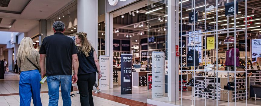 Grupa ludzi spacerująca w galerii handlowej, obok sklepu CCC. Jasne wnętrze i wystawy.