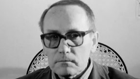 Zdjęcie przedstawia mężczyznę w okularach, z poważnym wyrazem twarzy, na tle jasnej ściany.