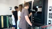 Na zdjęciu dzieci oddają opakowania do maszyny recyklingowej w punkcie zbiórki.