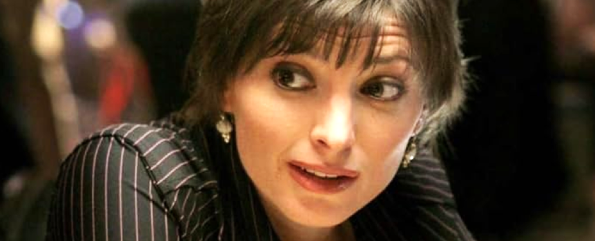 Na zdjęciu młoda kobieta o ciemnych włosach i okrągłych kolczykach, w eleganckiej bluzce.