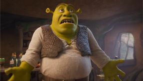 Shrek, zielony ogr z wyrazem zdziwienia, stoi w przytulnym pomieszczeniu.