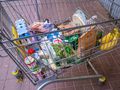 Koszyk na zakupy z różnymi produktami spożywczymi: napojami, chlebem, owocami, warzywami.