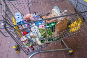 Koszyk na zakupy z różnymi produktami spożywczymi: napojami, chlebem, owocami, warzywami.
