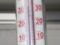Termometr stojący na tle okna, wskazujący temperaturę około 20 stopni Celsjusza.