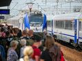 Tłum ludzi na dworcu, pociąg wjeżdżający na peron. Słoneczny dzień, niebo bez chmur.