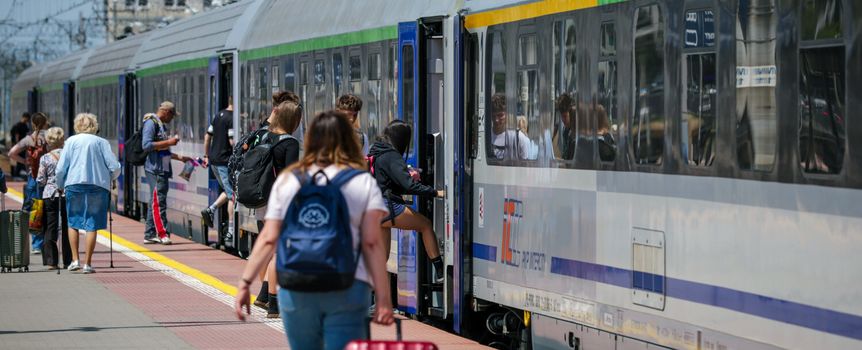 Tłum ludzi wsiadających do pociągu na stacji kolejowej w słoneczny dzień.